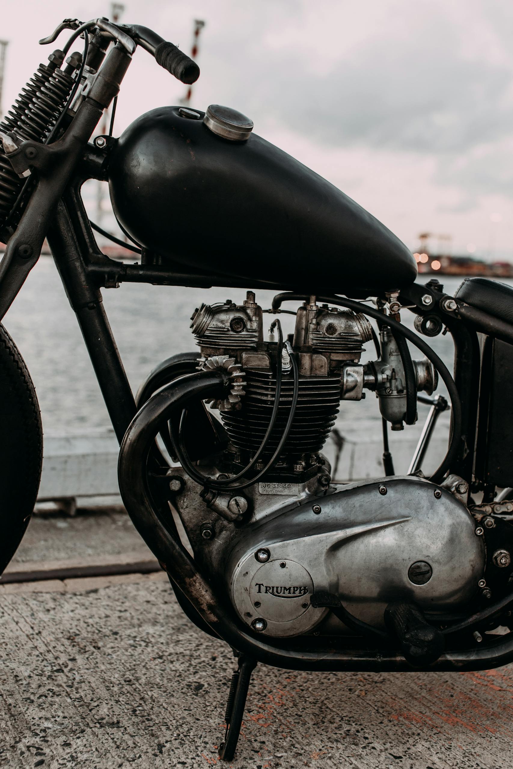 Close-up of a vintage motorcycle parked outdoors by a waterfront.